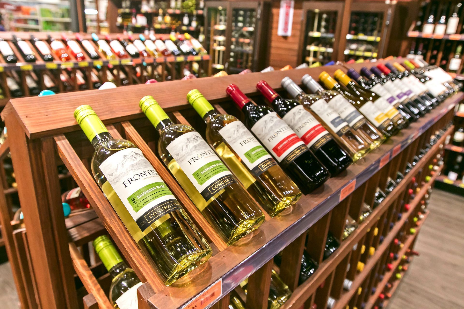 Botellas de vino exhibidas en estantes de madera en una licorería, con varias etiquetas y colores.