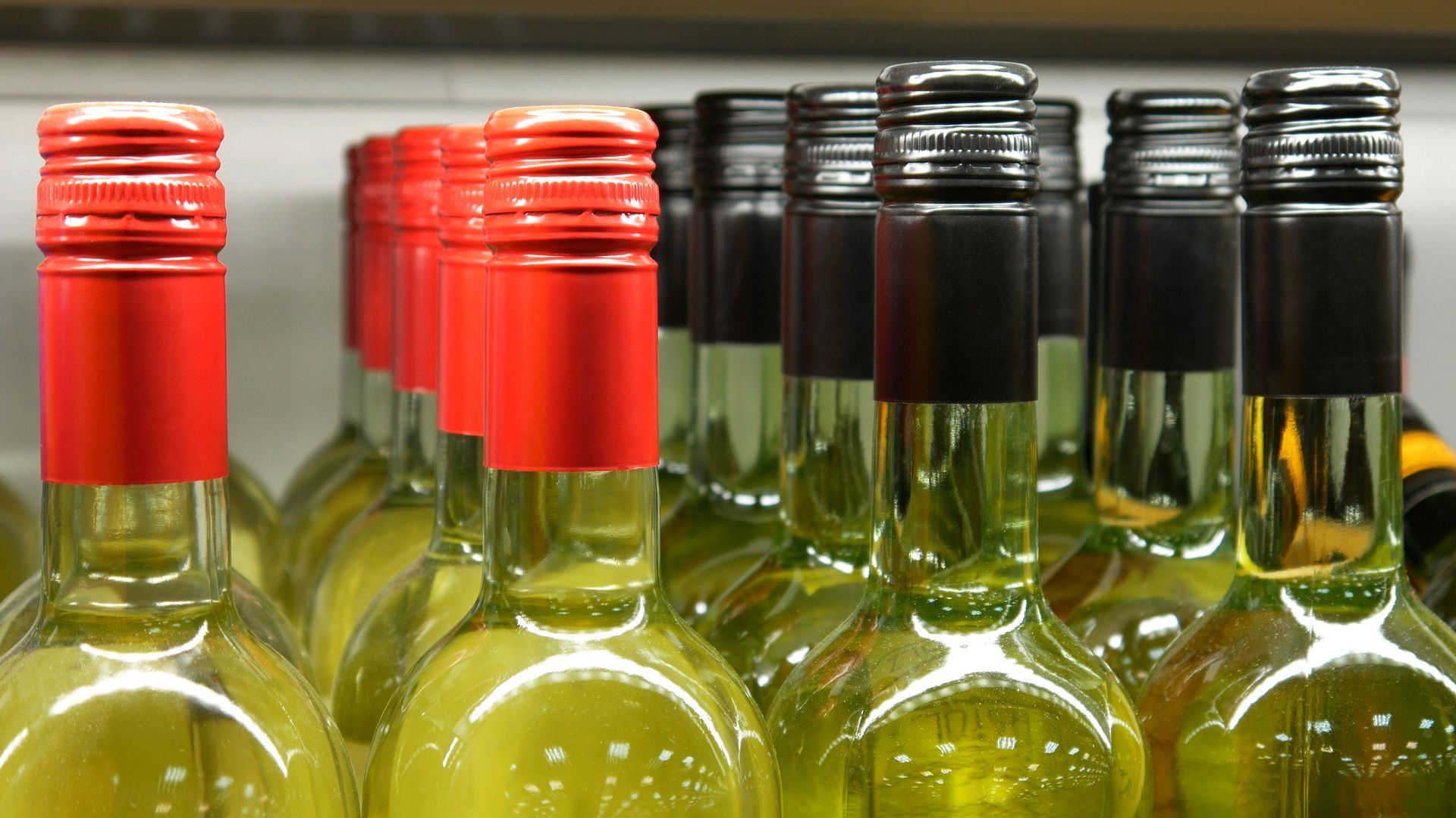 Botellas de vino blanco en fila, algunas con tapón rojo, otras con tapón negro.