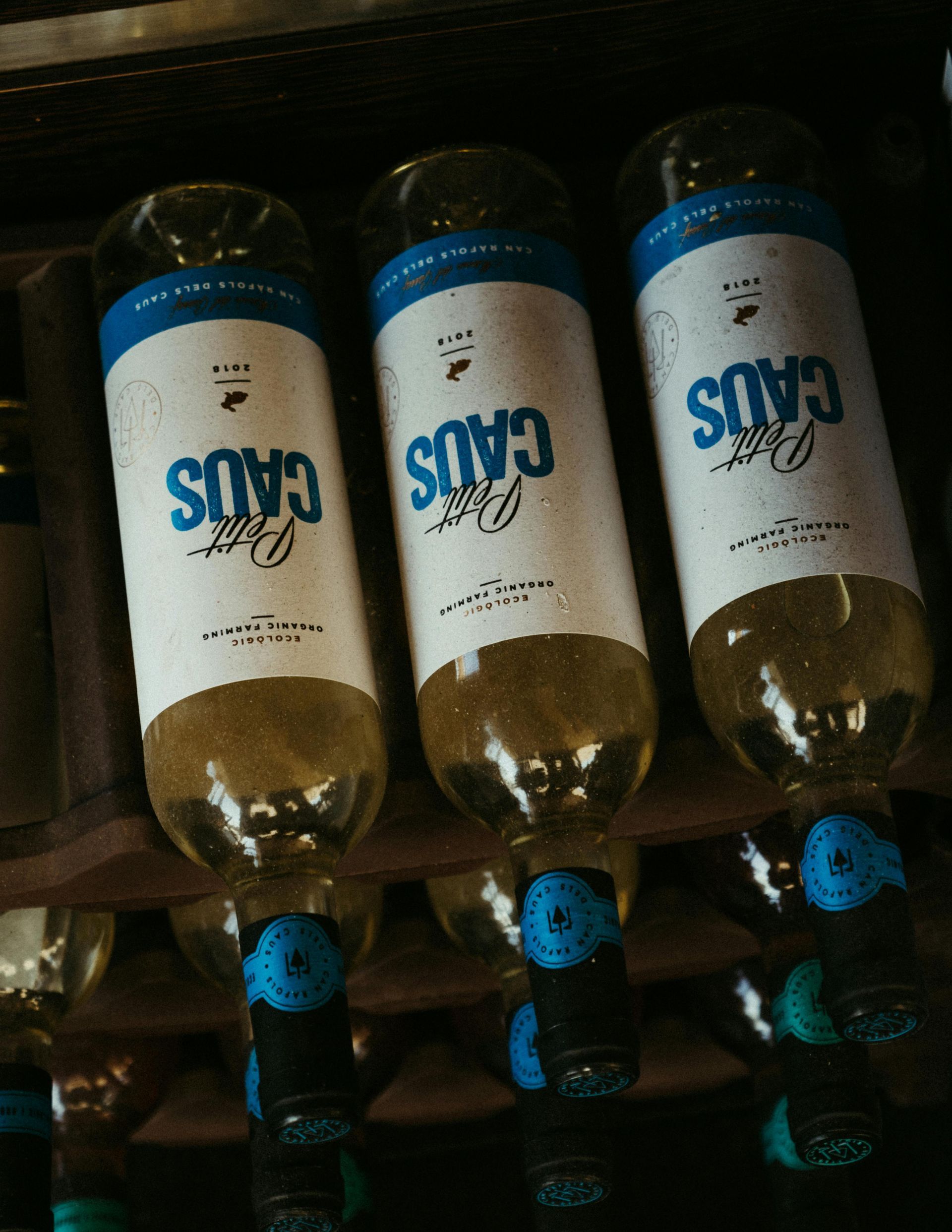 Tres botellas de vino con etiquetas azules y blancas en un estante de madera.