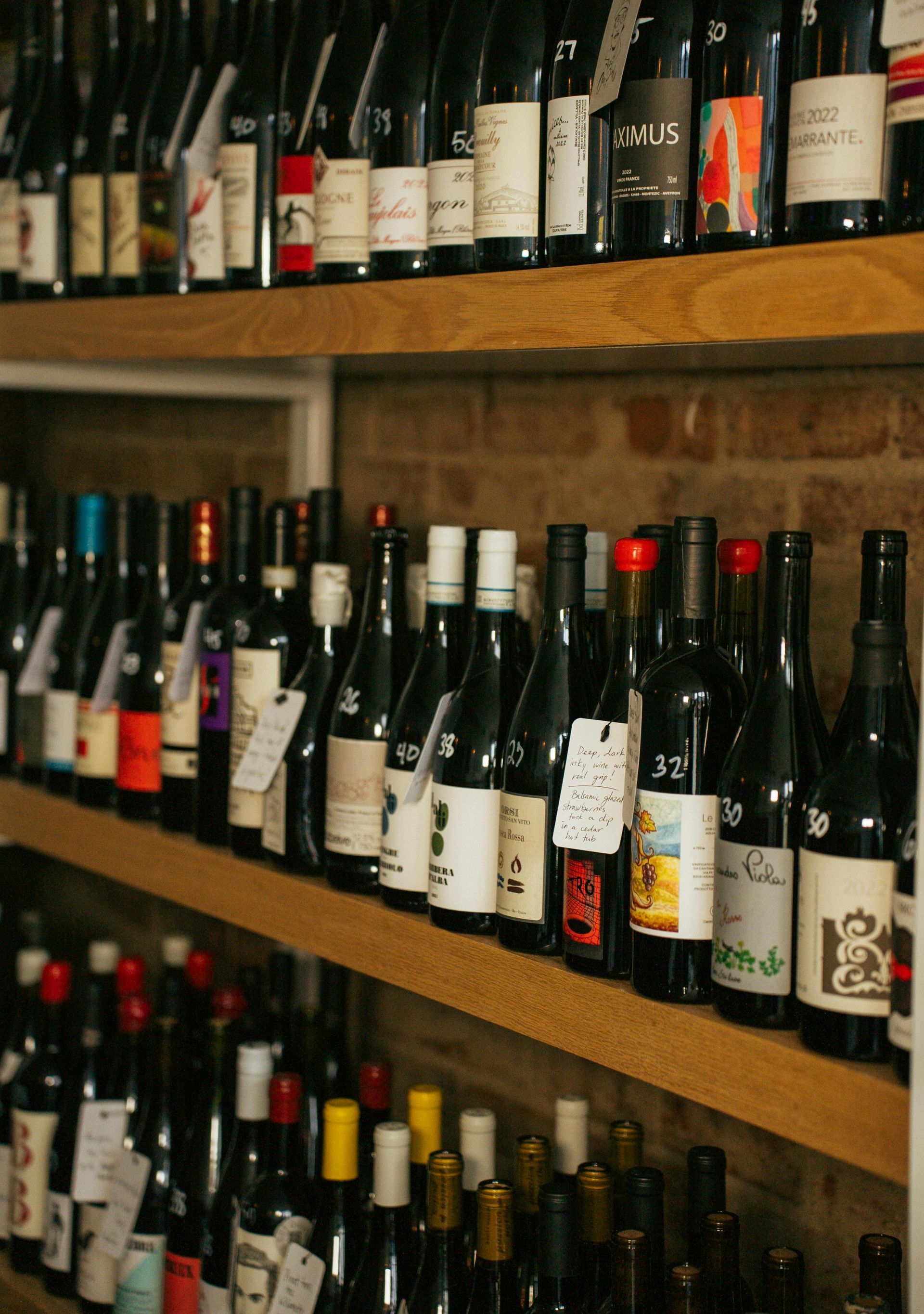 Botellas de vino en estantes de madera en una tienda, etiquetas visibles, fondo de ladrillo.