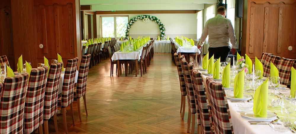 Ein langer Speisesaal mit Tischen und Stühlen, aufgestellt für einen Hochzeitsempfang.