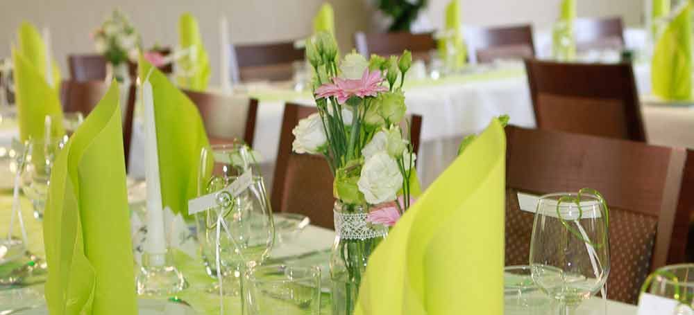 Ein für einen Hochzeitsempfang gedeckter Tisch mit grünen Servietten und Blumen in einer Vase.