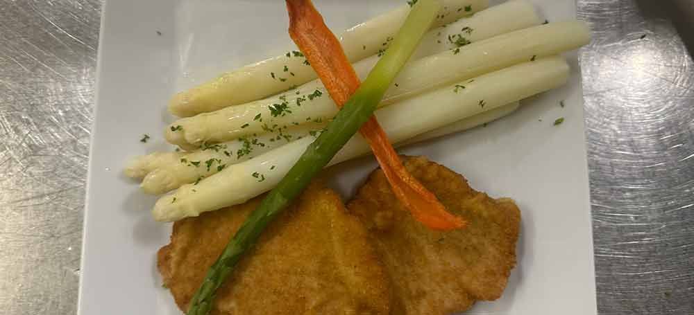 Ein weißer Teller mit weißem Spargel, Schinken und Zitrone.