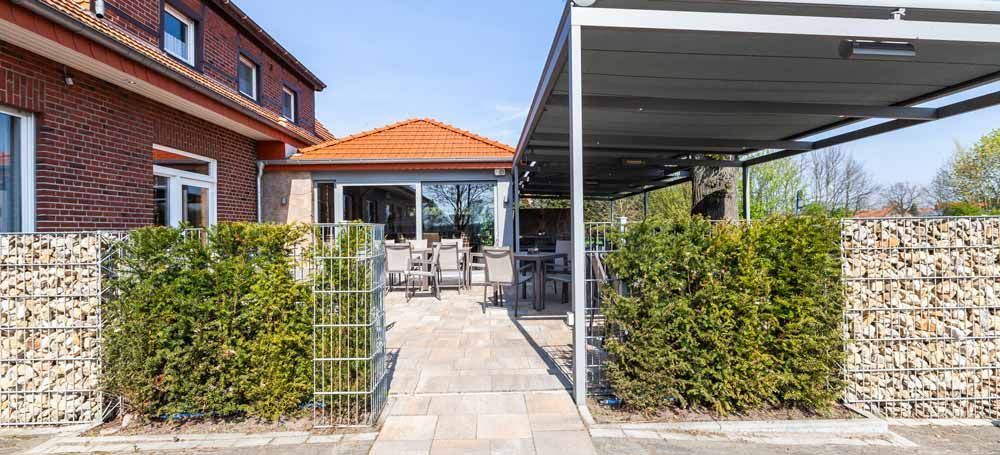 Ein Backsteingebäude mit einer Terrasse und einem Vordach davor.