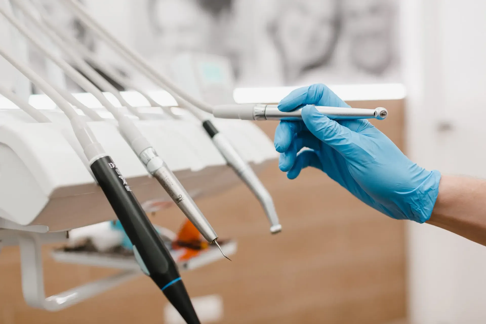 Una mano enguantada de azul selecciona un instrumento dental blanco de un estante en una clínica.