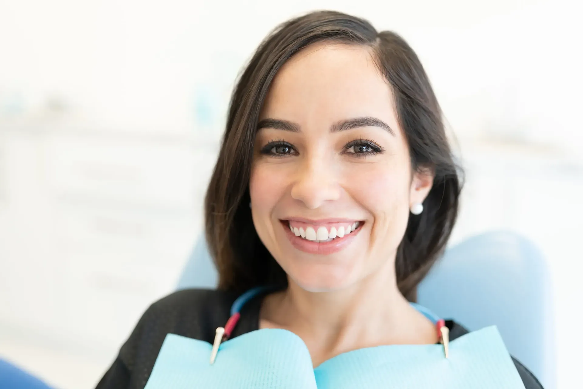 Paciente sonriente en una silla dental con un babero turquesa y herramientas dentales cerca.