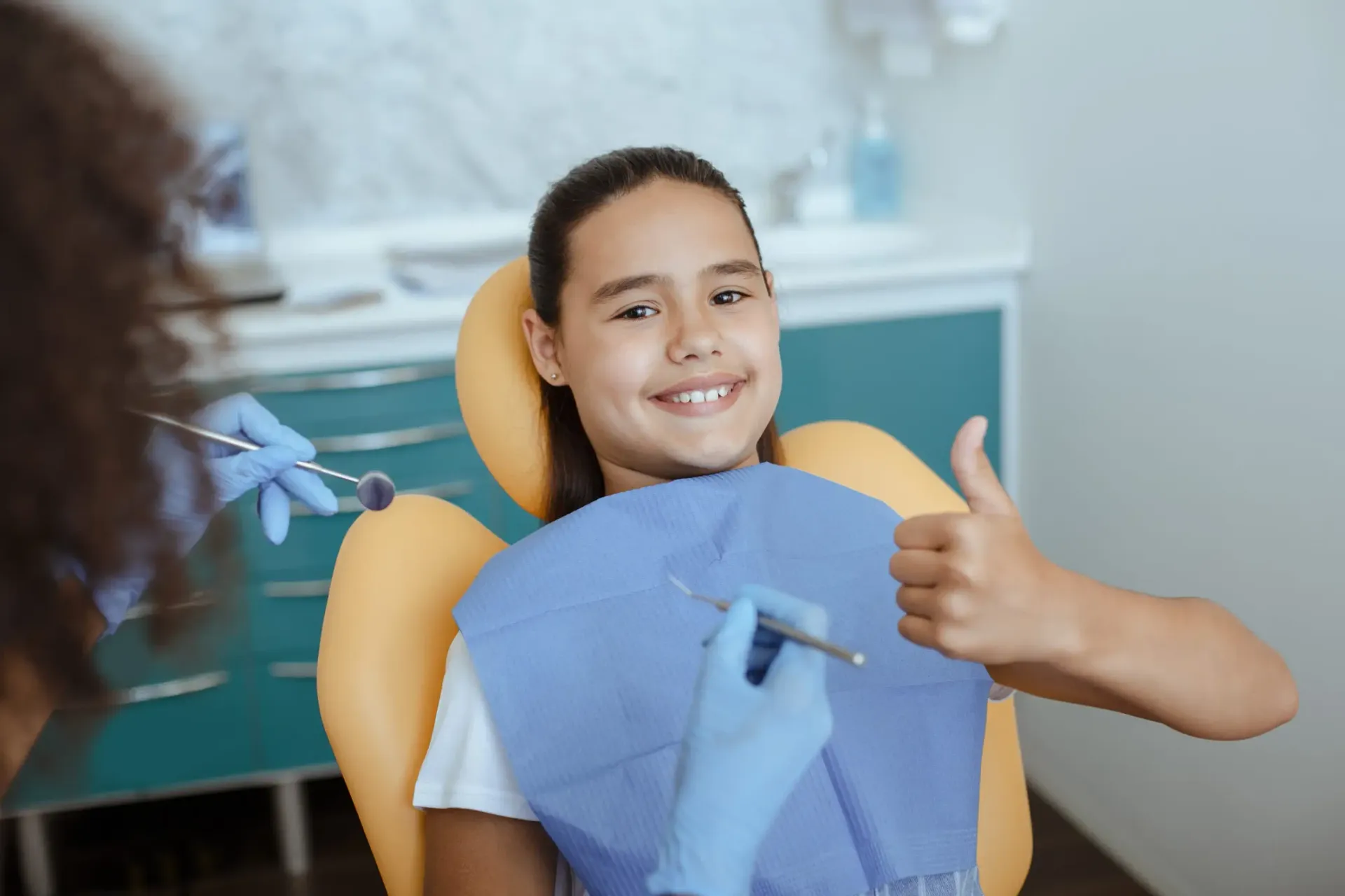 Un niño sonriente en la silla del dentista levanta el pulgar durante una revisión.