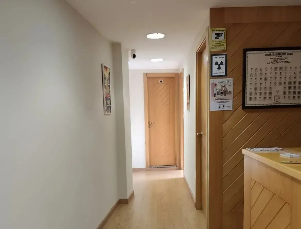 Pasillo luminoso con suelo de madera, paredes blancas, puertas de madera y un mostrador a la derecha.