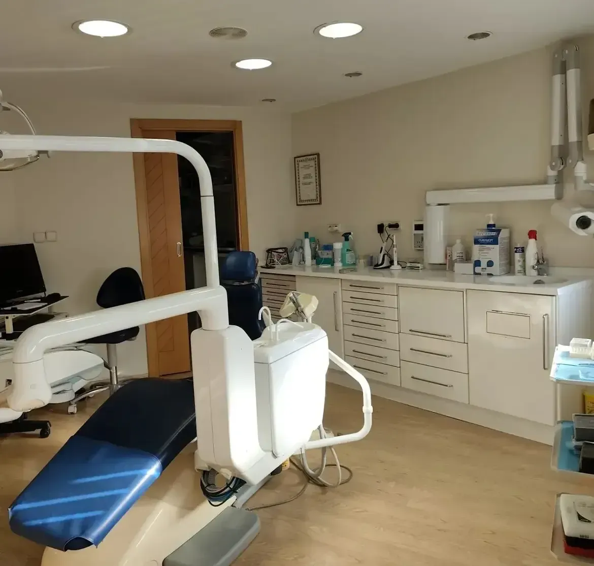 Sala de tratamiento dental con sillón, luz de techo y armarios blancos a lo largo de la pared.