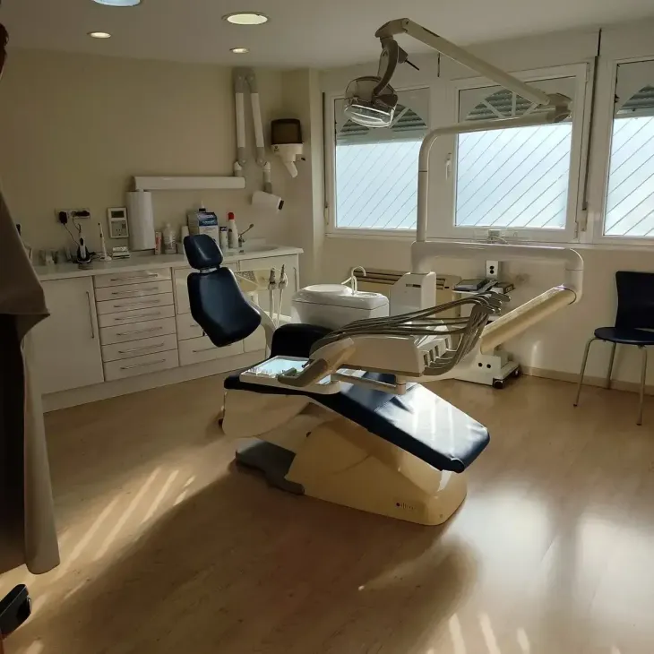 Consultorio dental con sillón de exploración, luz cenital, armarios y grandes ventanales que dejan entrar la luz natural.