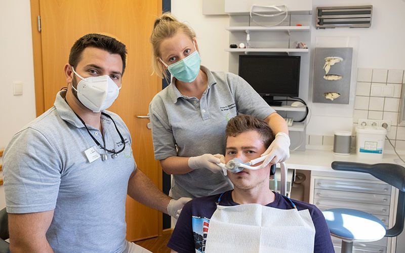 Ein Mann sitzt in einem Zahnarztstuhl, während zwei Zahnärzte an seinen Zähnen arbeiten.