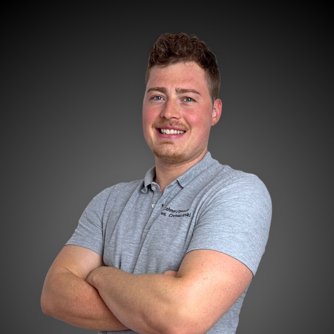 Ein Mann in einem grauen Poloshirt steht mit verschränkten Armen da.