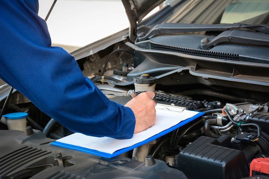 Un mecánico está escribiendo en un portapapeles debajo del capó de un automóvil.