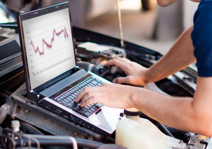 Un hombre está trabajando en un automóvil con una computadora portátil.