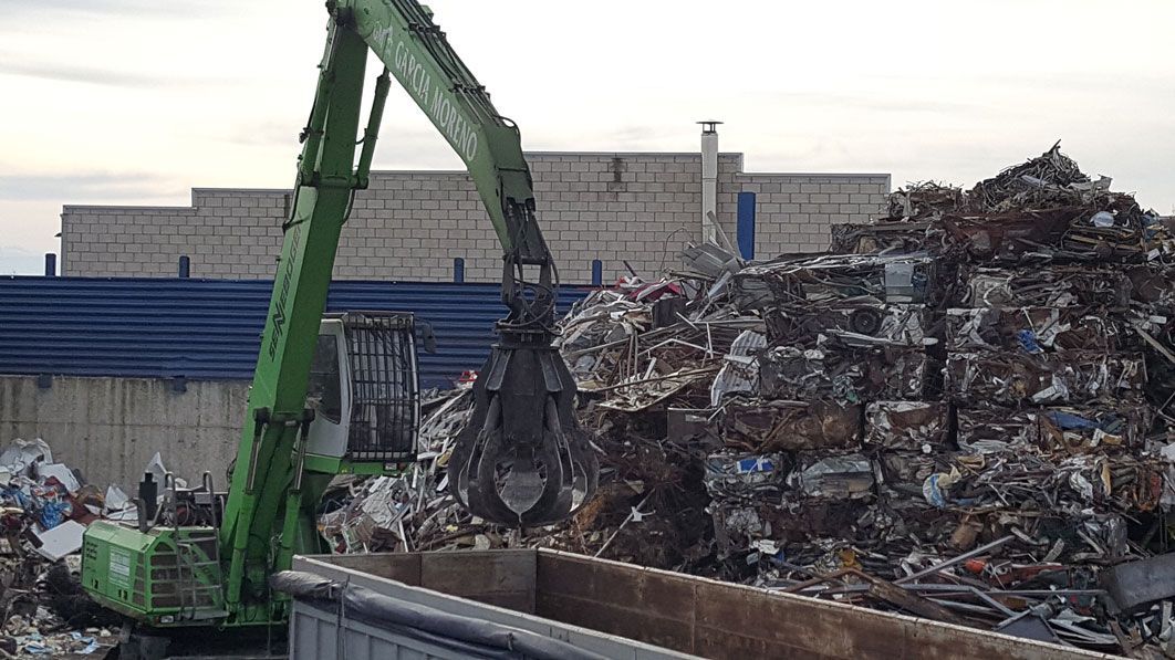 Una grúa verde está cargando una pila de chatarra en un camión.
