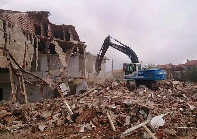 Una excavadora azul y blanca está demoliendo un edificio.