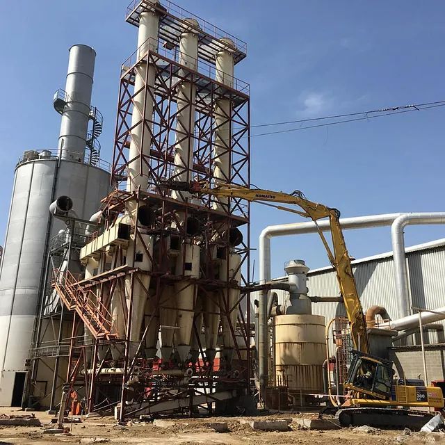 Un gran edificio industrial con una excavadora amarilla delante.