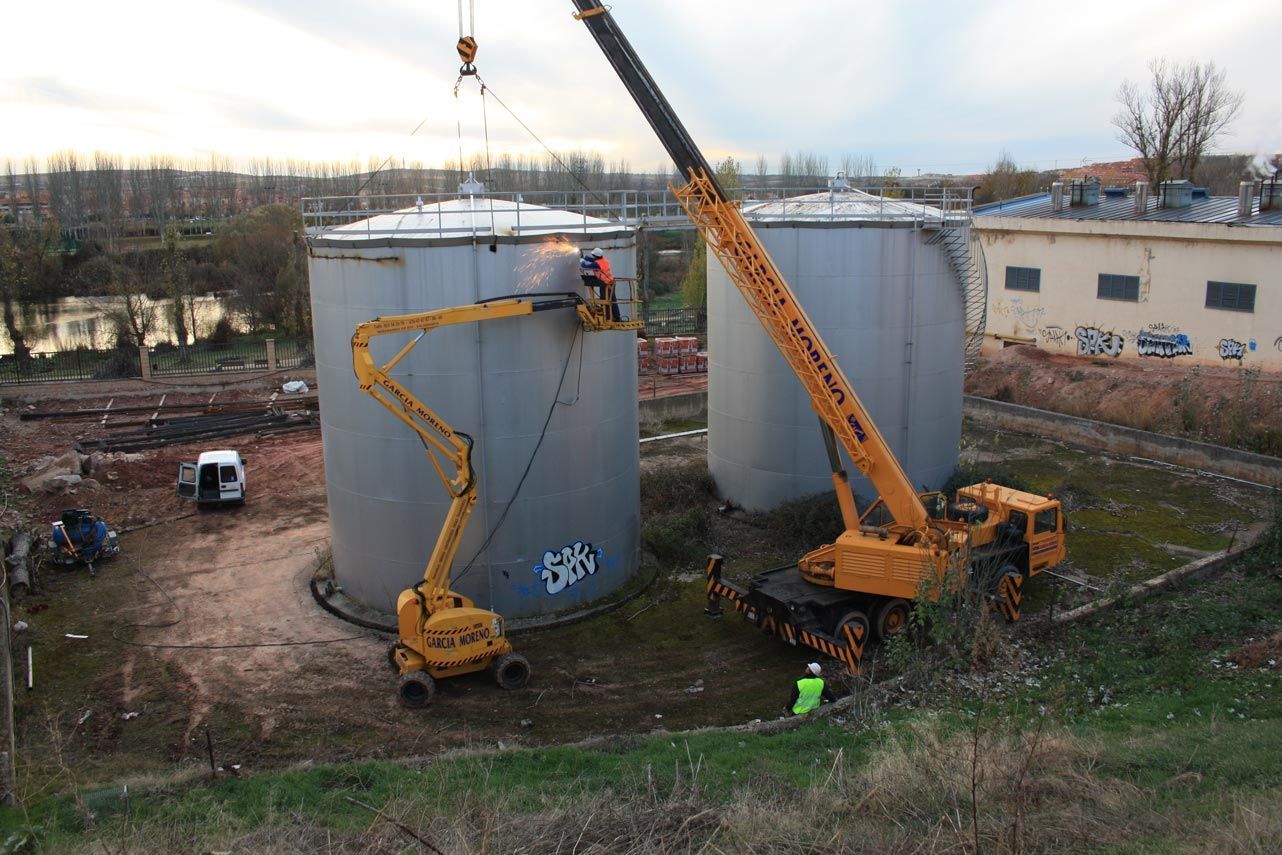 Una grúa está levantando un gran tanque de metal en un campo.