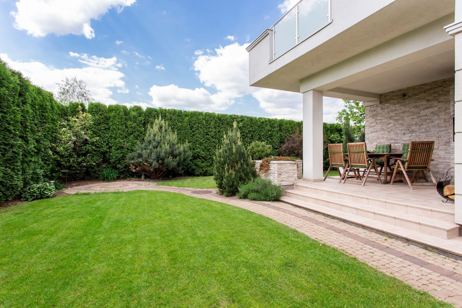 Terrasse moderne dans le jardin avec sièges en bois, marches en pierre, pelouse verte et hautes haies.