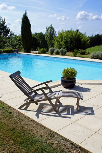 Chaise longue au bord de la piscine sur une terrasse ensoleillée, près d'une piscine bleue et d'une plante en pot