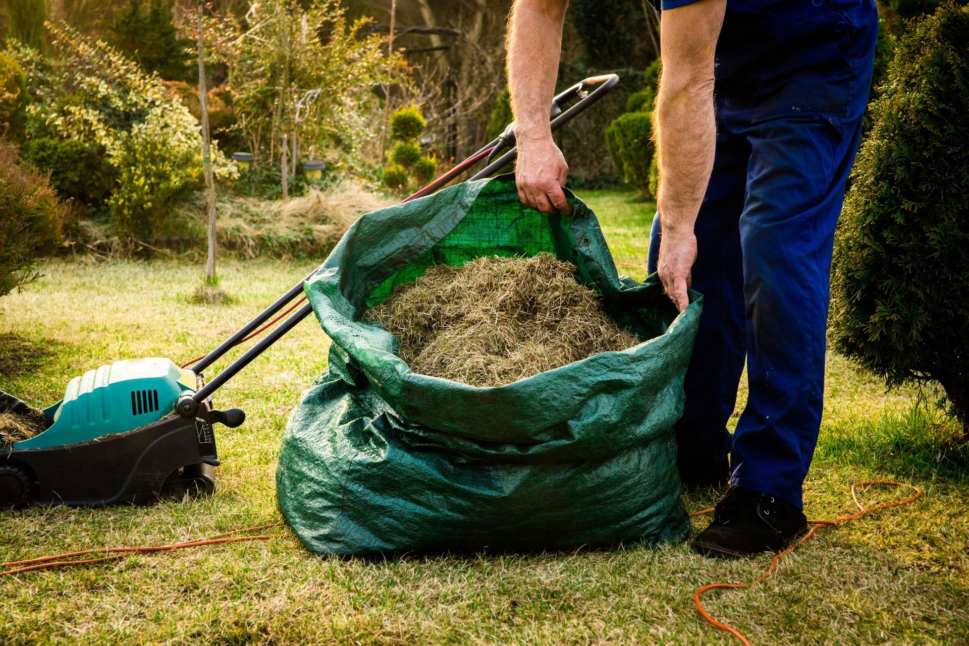 Une personne remplit un sac à déchets verts avec des tontes de gazon dans un jardin.