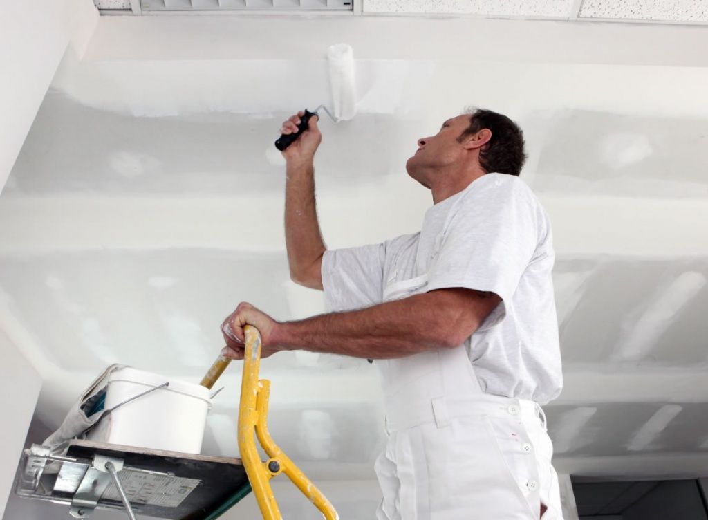 Mann streicht eine Zimmerdecke
