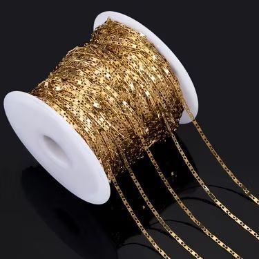 Chaîne dorée enroulée sur une bobine blanche, posée sur une surface sombre.