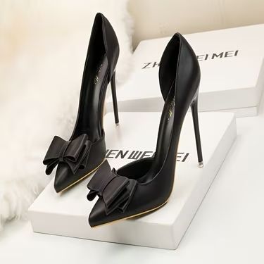 Chaussures noires à talons hauts ornées d'un nœud, posées sur une surface blanche.