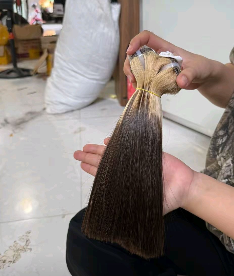 Une personne tenant des mèches d'extensions de cheveux ombrées, allant du brun foncé au blond clair, dans un décor lumineux.