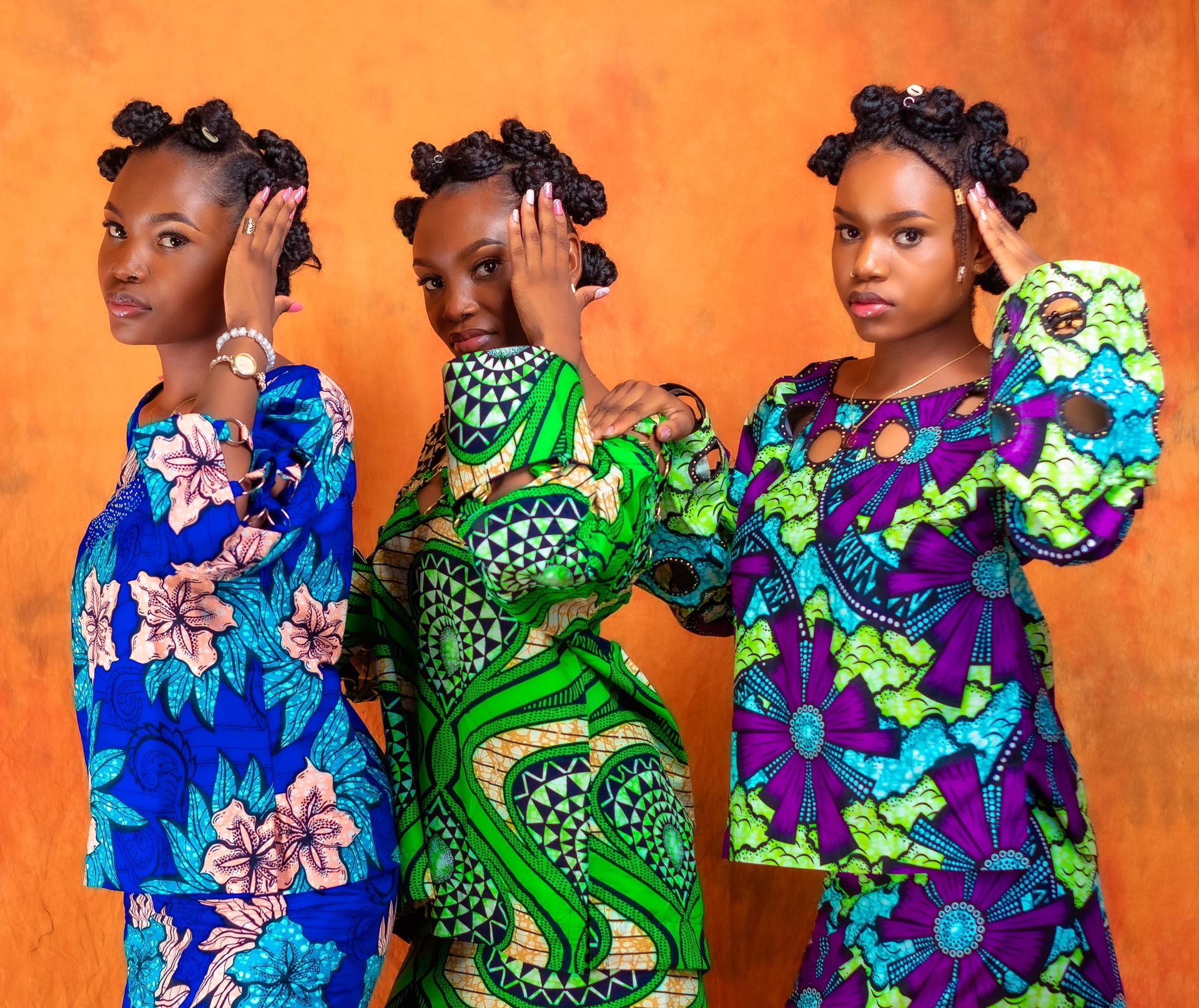 Trois personnes vêtues de tenues à motifs assortis, posant les mains près de la tête sur un fond orange.