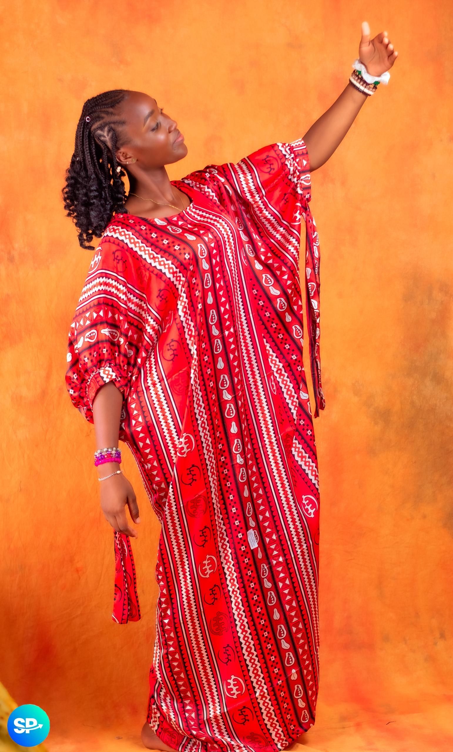 Femme en robe à motifs rouges et blancs, bras levés, sur fond orange.