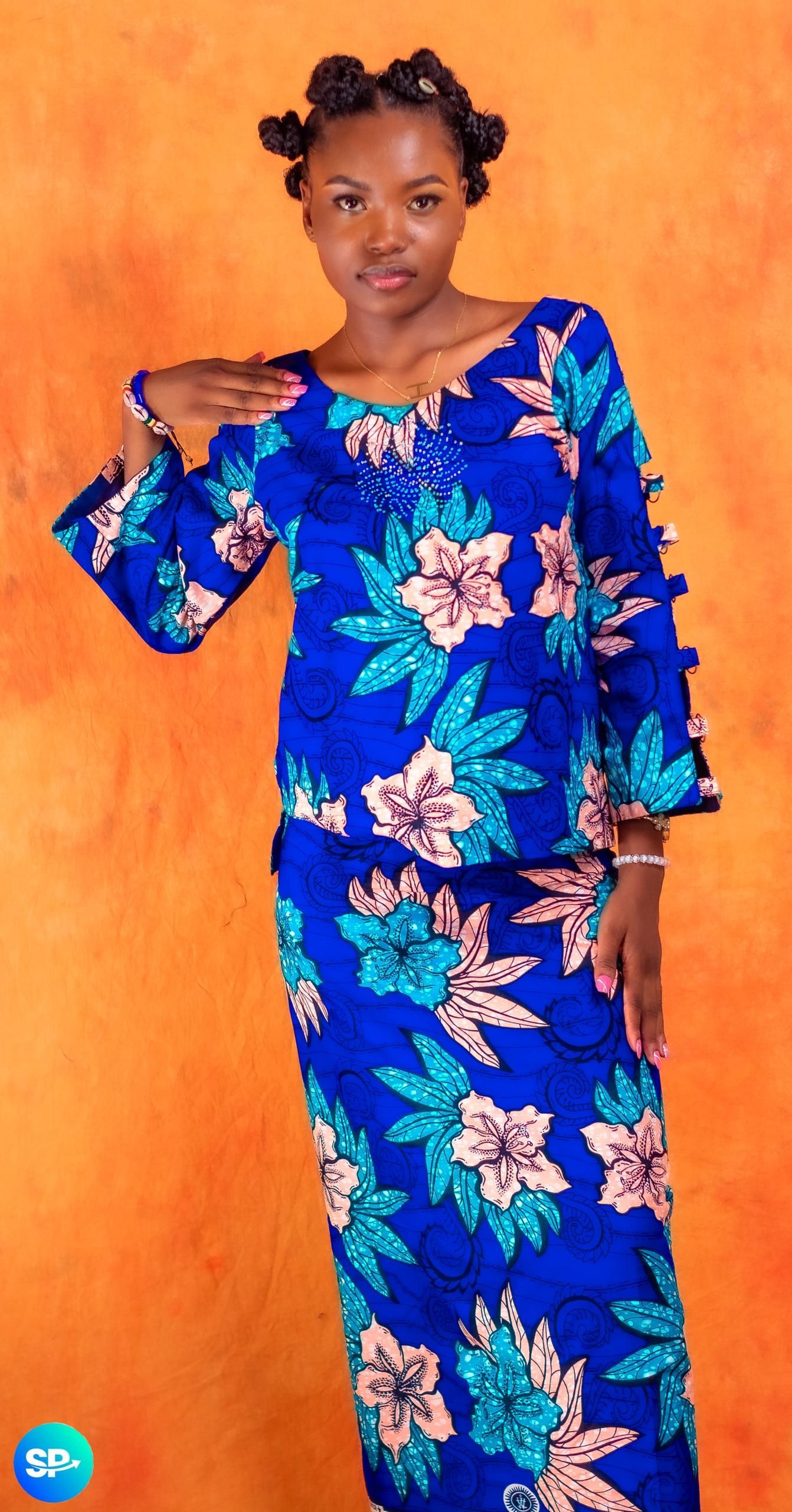 Femme en tenue fleurie bleue, debout, sur fond orange.