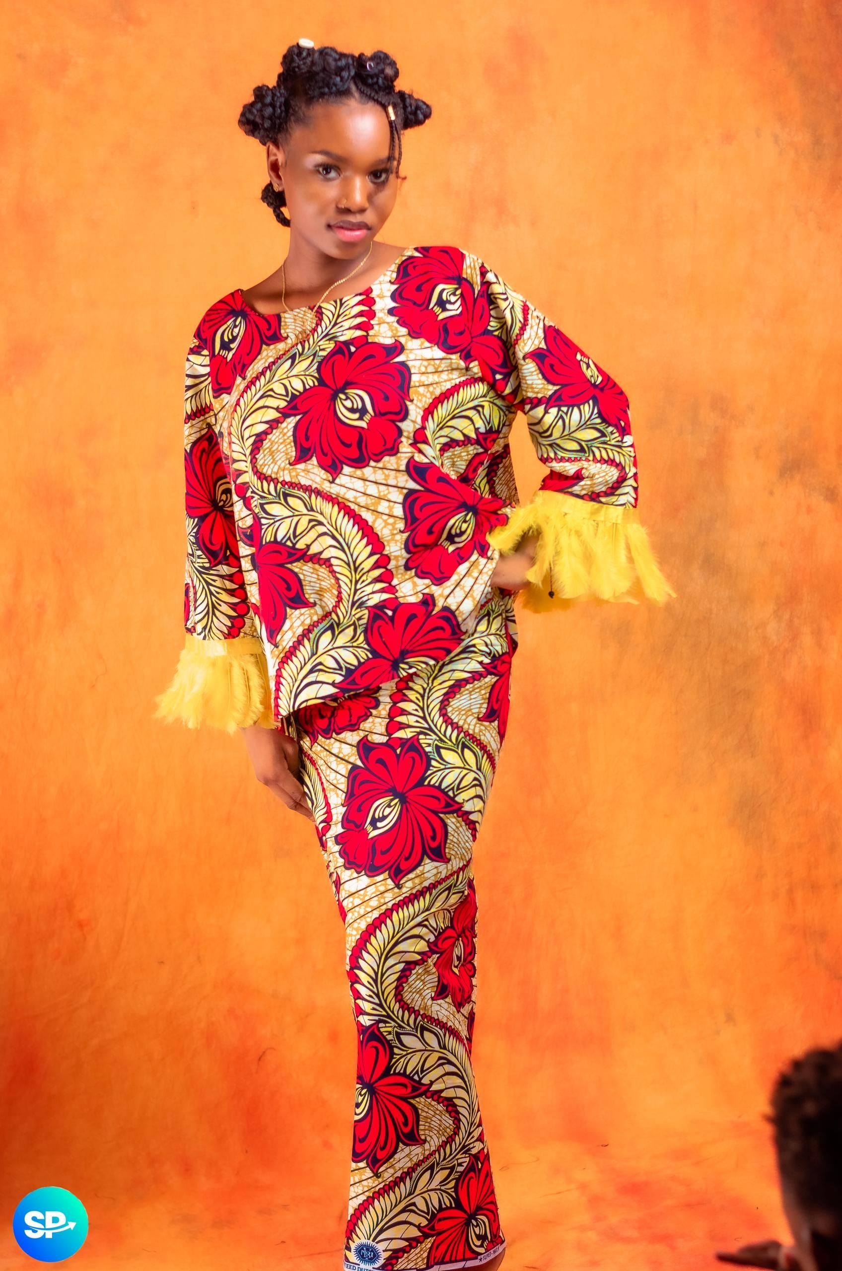 Femme en robe rouge à imprimer floral, debout, la main sur la hanche, sur fond orange.