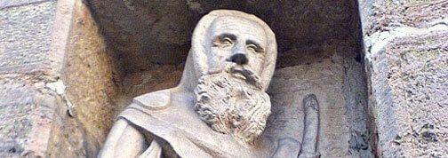 Auf einer Steinmauer sitzt die Statue eines Mannes mit Bart.