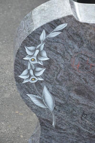 Eine Nahaufnahme eines Grabsteins mit Blumen und Blättern darauf.