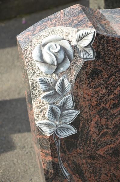 Ein Grabstein mit einer geschnitzten Rose und Blättern darauf.