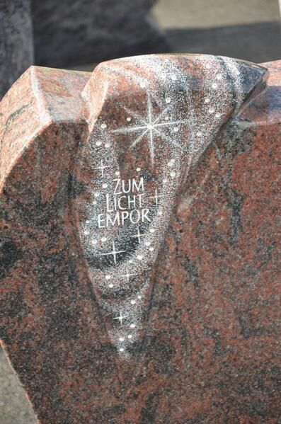 Eine Nahaufnahme eines Grabsteins mit einem eingemeißelten Kreuz.