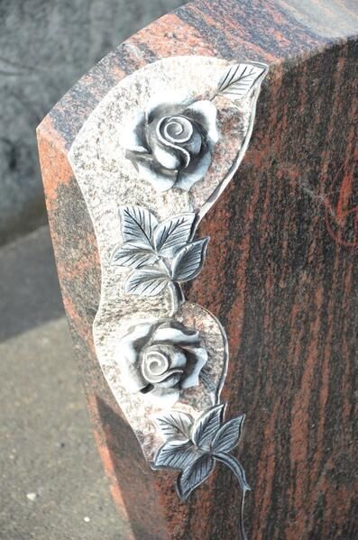Eine Nahaufnahme eines Grabsteins mit Rosen und Blättern darauf.