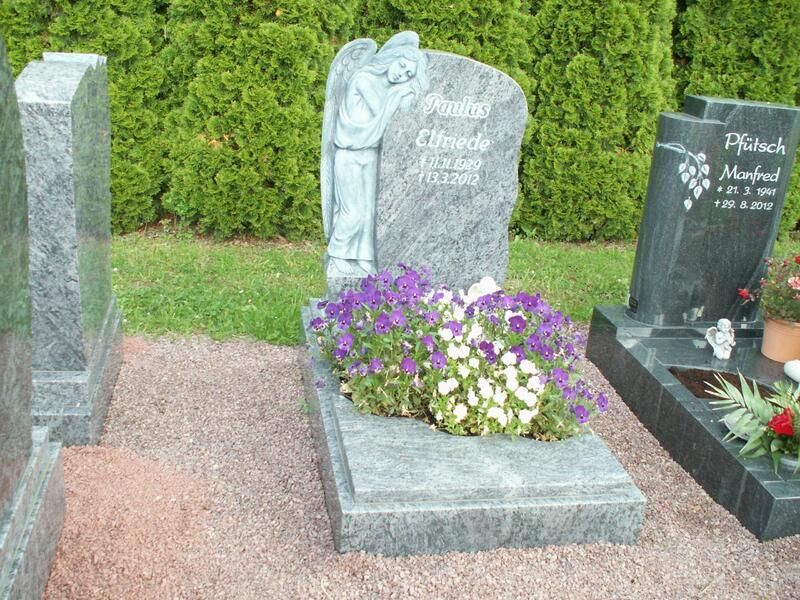 Ein Grab mit lila Blumen und einer Engelsstatue