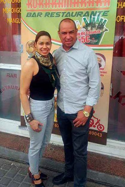 Dos personas paradas afuera de un restaurante: una mujer con una camiseta negra y jeans