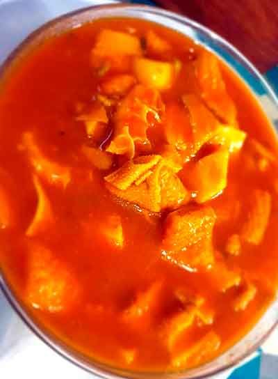 Primer plano de un tazón de guiso de naranja con trozos de comida, posiblemente callos o carne, y verduras.