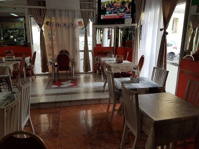 Interior de restaurante con mesas, sillas, ventanas y televisión.