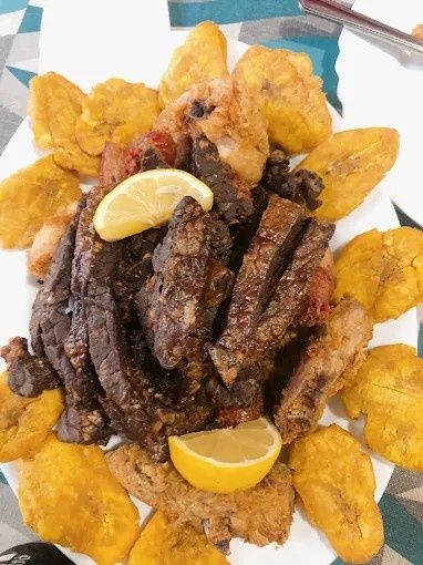 Plato de carne frita y plátanos, con guarnición de limón.