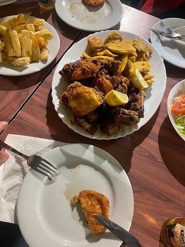 Mesa con platos de comida frita y ensalada; manos utilizando cubiertos.