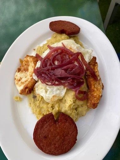 Plato de mofongo con huevos fritos, cebolla roja, queso y salami frito.