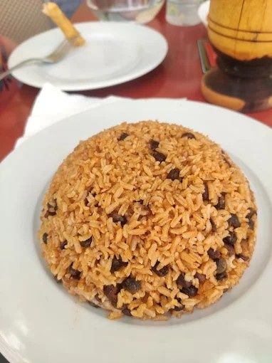 Arroz y frijoles en un plato blanco. Al fondo, un tenedor, un plato pequeño y un recipiente de madera.