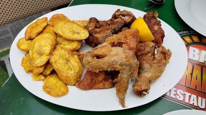 Plato de pollo frito y plátanos con rodaja de limón.