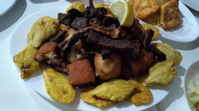 Plato de carne frita, plátanos y papas, aderezado con limón.