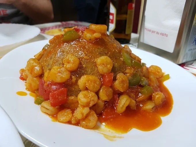 Plato de comida: Montículo de arroz cubierto con camarones y salsa de tomate.