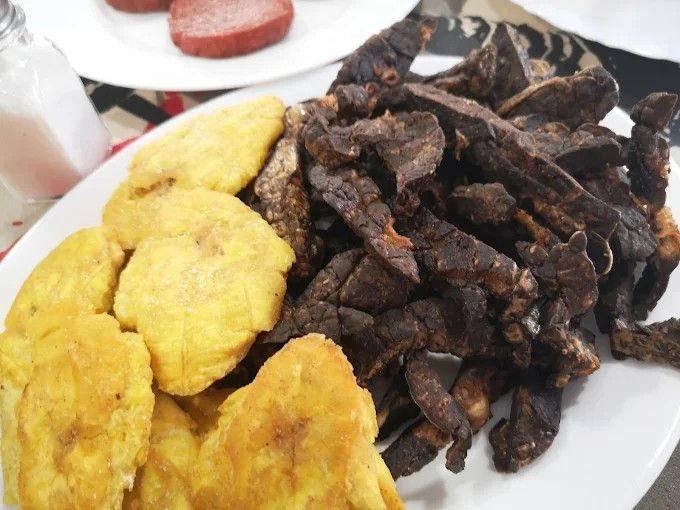 Plato con plátanos fritos y carne seca, y salchicha en plato aparte.